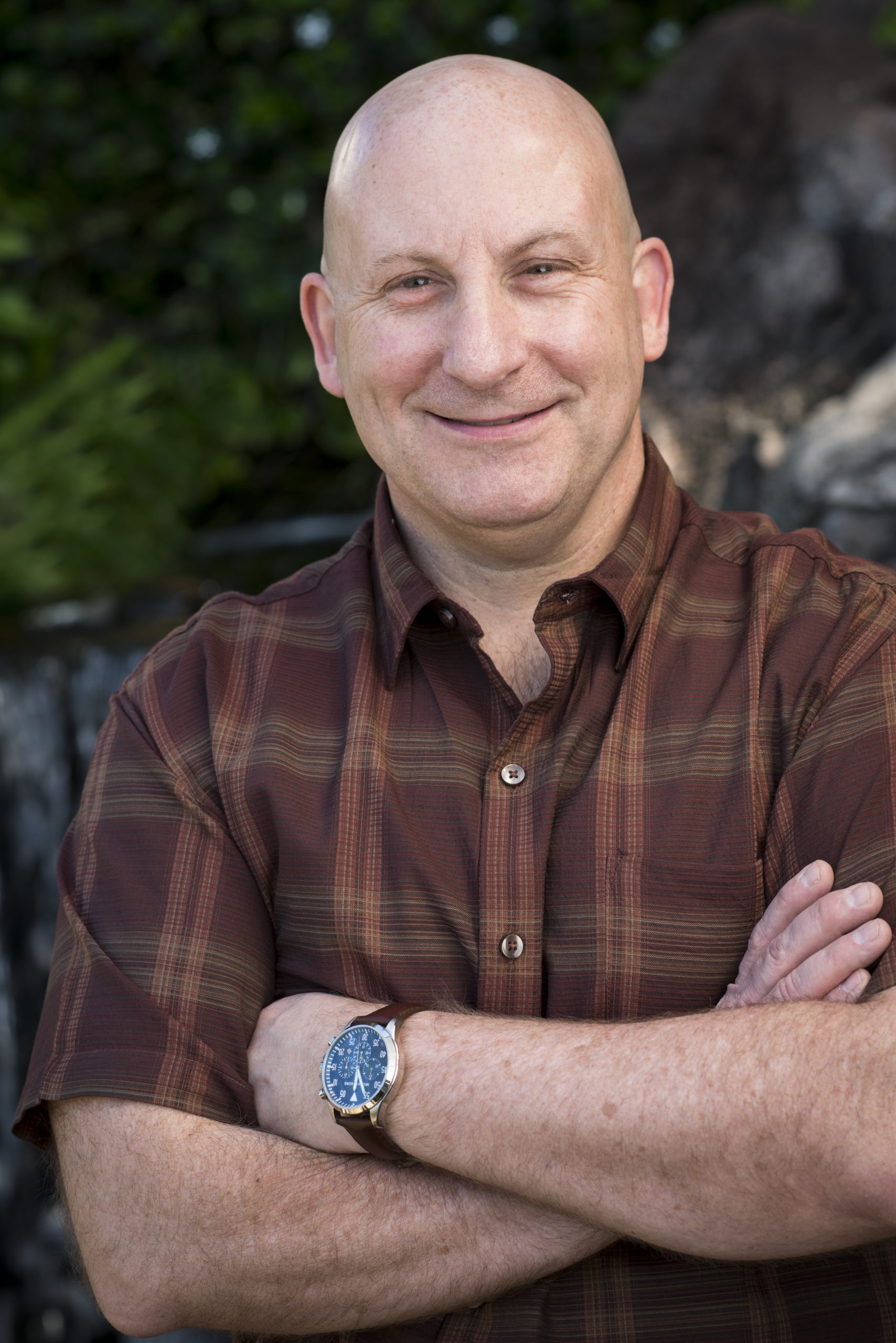 Man in plaid brown button up (Eric Linder) poses in front of a blurred outdoor background.