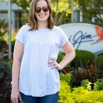 Woman  in a white shirt and sunglasses (Veronica Quiroz) poses in front of the Maui Jim sign
