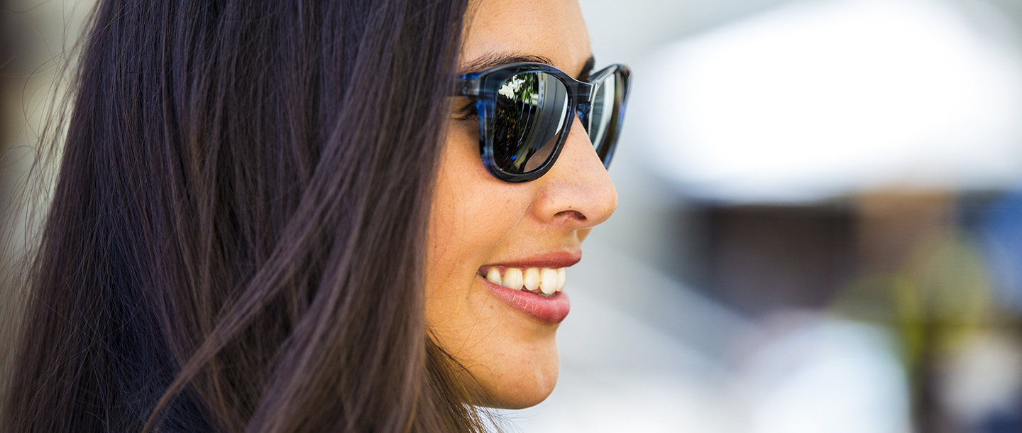 Woman in blue and black sunglasses smiling in front of a blurred background